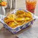 A basket of nachos with Better Balance vegan cheese sauce and jalapenos on a table with a soda.