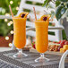 Two Acopa Endure Tritan plastic hurricane glasses of orange juice with straws and fruit slices on a table.