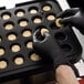 A black gloved hand using a Pavoni Cookmatic Pastry / Tartlet Heated Press to make small round pastries.