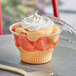 A clear plastic dessert cup with orange and white dessert and a flat lid.