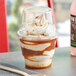 A Choice clear plastic dessert cup of ice cream with whipped cream and caramel sauce.
