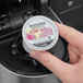 A hand holding a small round container with a Bigelow Benefits Lemon and Echinacea Herbal Tea K-Cup pod in it.