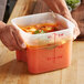 A person holding a Cambro FreshPro translucent food storage container of soup.