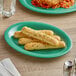 A green Acopa Foundations melamine platter with bread sticks and spaghetti on a table.