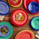 An Acopa purple melamine tray holding a plate of food on a table with a stack of colorful plates.