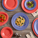 An Acopa Foundations orange melamine salad bowl on a wood table with a variety of colorful plates and bowls.