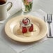 A tan Acopa Foundations melamine plate with a red velvet cinnamon roll on it on a table with a white mug and flowers in a glass.