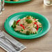 A green Acopa Foundations melamine plate with pasta, broccoli, and vegetables with a fork.