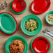 A wood table with green Acopa melamine plates and red and green bowls of food.