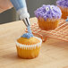 A person using a Wilton #233 piping tip to decorate a cupcake with purple frosting.