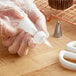 A person in gloves using a Wilton plastic tube to pipe white frosting.