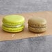 Two Coco Bakery pistachio macarons on a brown paper.