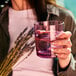 A woman holds a Tossware Reserve Go-To Blush Rocks Glass filled with water.