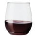 A Tossware plastic vino glass filled with dark liquid on a white background.