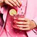 A woman in a pink suit holding a Tossware plastic rocks glass with a straw and a lime slice in pink liquid.
