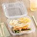 A sandwich with meat and cheese and potato chips in a Genpak clear plastic hinged container.