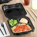 A black Genpak 3-compartment container with food inside and a black fork.