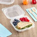 A Genpak clear plastic hinged container with a sandwich, fruit, and bread with sprouts inside.