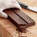 A gloved hand cutting a TCHO 68% Dark Chocolate Bar with a knife.