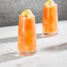 Two Della Luce Dion beverage glasses filled with orange liquid and ice, garnished with lemon slices.