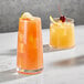 Two Della Luce Dion beverage glasses filled with orange juice and garnished with a lemon slice and a cherry.