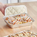 A hand holding a Baker's Lane foil tray of cinnamon rolls with white frosting.