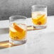 Two Della Luce double old fashioned glasses of whiskey with ice and orange slices.