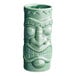 A close-up of a green ceramic Acopa Tiki Mug with a face carved on it.