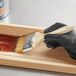 A person in black gloves using a Midwest Rake 3" Bristle Chip Brush to paint a wooden box.