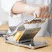 A person using a Vollrath CubeKing cheese slicer to cut cheese.
