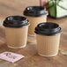 A group of brown Choice paper hot cups with black lids on a table.