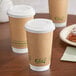 A group of EcoChoice brown paper coffee cups with white lids on a table.