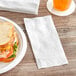 A plate of a sandwich and Tork white dinner napkin on a table.