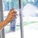 A person using Noble Chemical Kleer View glass cleaner to spray a window.