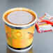 A Huhtamaki paper soup cup with a lid filled with soup on a counter.