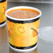 Two Huhtamaki paper soup cups on a counter, one with soup in it and a design on it.