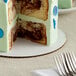 A slice of cake with chocolate frosting and blue sprinkles on a Baker's Mark white corrugated cake circle.