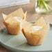 Two Baker's Mark unbleached natural kraft tulip baking cups with cupcakes inside on a white plate.