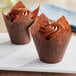 Two chocolate cupcakes in Baker's Mark brown tulip baking cups on a white surface.