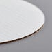 A close up of a Baker's Mark white corrugated cake circle with a curved edge.