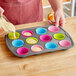 A person pouring batter into pink, blue, and white Bakelicious silicone baking cups.