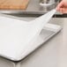 A hand placing a Baker's Lane silicone coated parchment paper sheet onto a baking sheet.