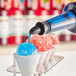 Blue Hawaiian shaved ice syrup being poured onto a red and blue snow cone.