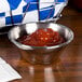 An American Metalcraft stainless steel sauce cup of red sauce on a table.