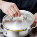 A hand holding a silver Vollrath Miramar low dome lid over a pot.
