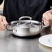 A chef using a Vollrath Miramar low dome lid on a pan on a table.