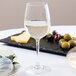 A Stolzle white wine glass on a table with a plate of olives and cheese.