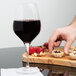 A hand reaching for a Stolzle Bordeaux wine glass filled with wine on a table with food.