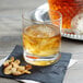 A Stolzle New York double old fashioned glass filled with amber liquid, ice, and nuts.