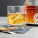 A Stolzle New York Rocks glass of whiskey with ice on a table.
